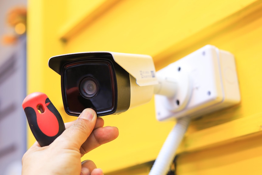 A small security camera being installed on a yellow wall