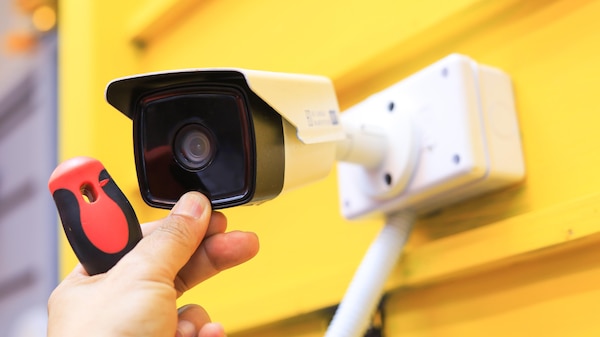 A small security camera being installed on a yellow wall