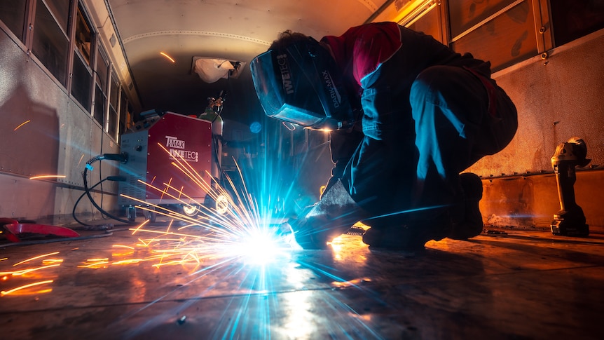 A welder wears a helmet and operates a sparking tool