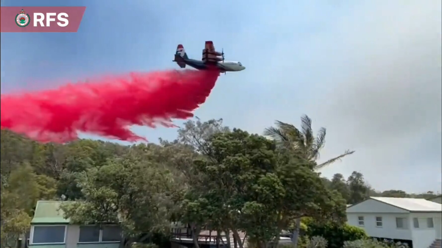 A large plane drops red fire retardant onto a bushland 