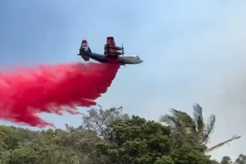 A large plane drops red fire retardant onto a bushland 