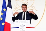 French President Emmanuel Macron stands at a lecturn with the French flag on the left behind him.