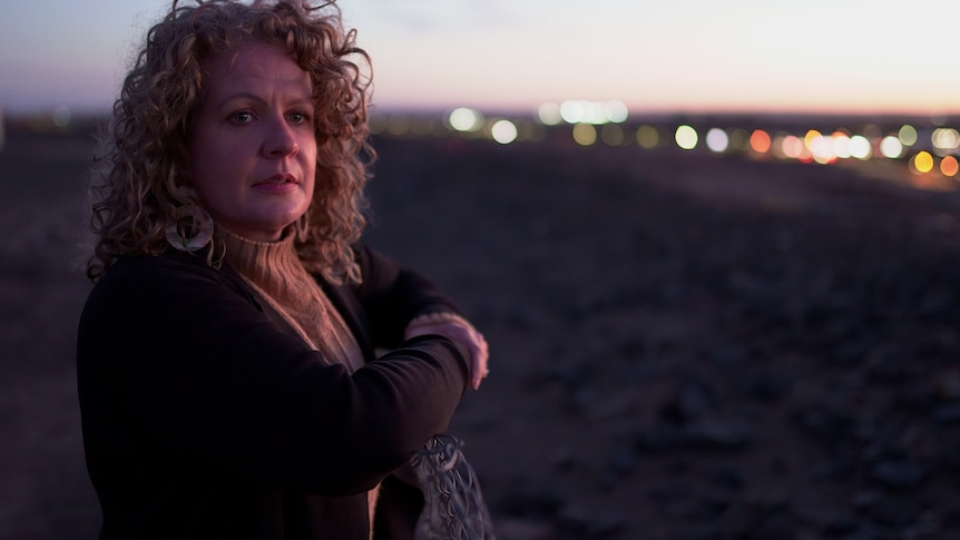 A woman stands outside leaning on a fence.