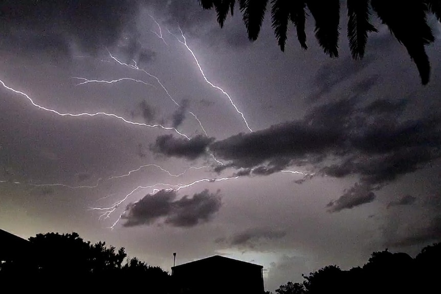 Lightning strikes across a grey sky above a house.