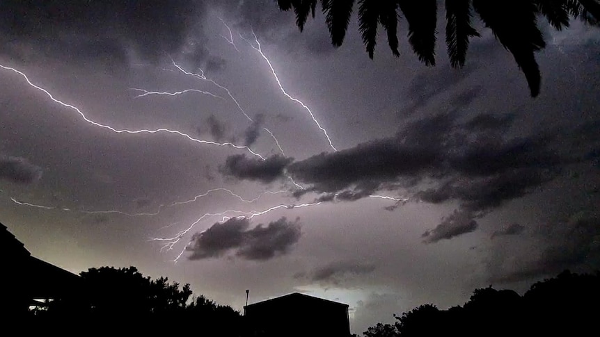 Lightning strikes across a grey sky above a house.