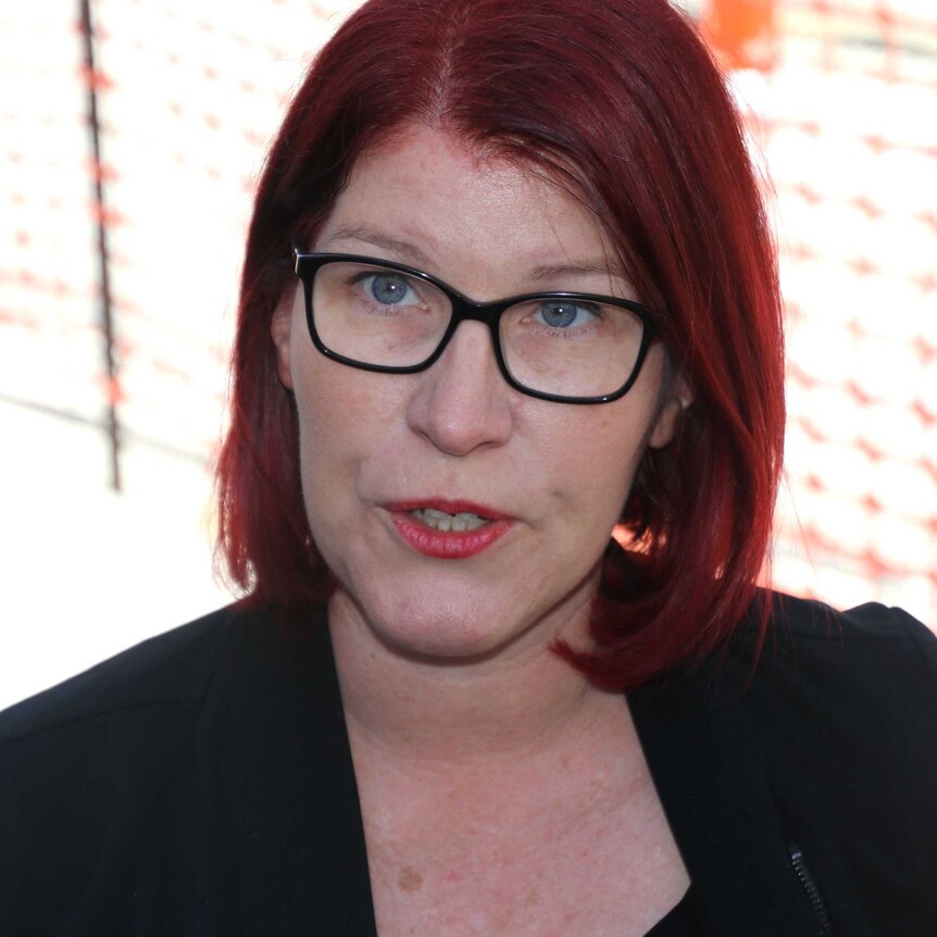 A close up of a red haired woman with glasses with sunshine and orange meshing in the background.