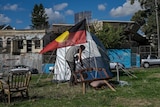 Neil Owen ducks under the Aboriginal Flag outside his tent