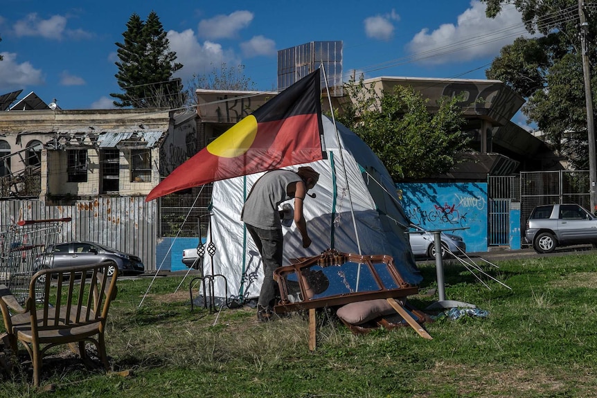 Neil Owen ducks under the Aboriginal Flag outside his tent