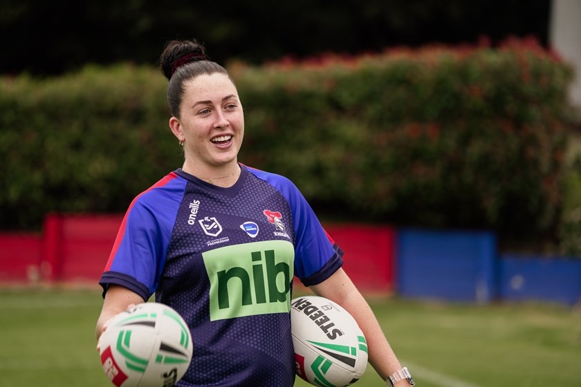 Woman standing on field holding two footballs.