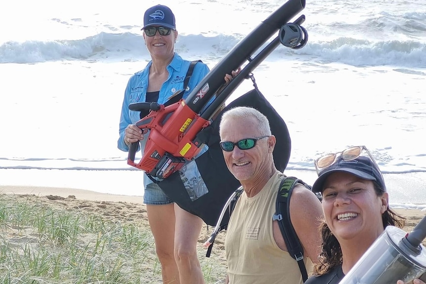 Karen Anderson with large blower vacuum and a man and woman stand on beach