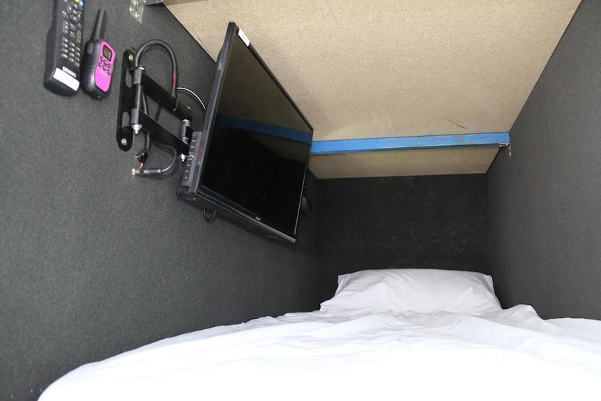 close up of a bed with white sheets walls on each side and a flatscreen TV on left wall