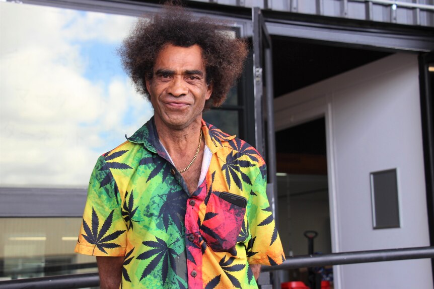 A man in a colourful shirt with an afro hairstyle smiles at the camera.