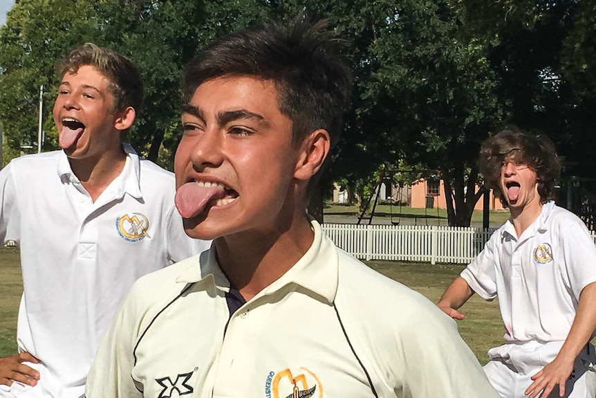 Three boys in cricket whites with their tongues out performing the haka