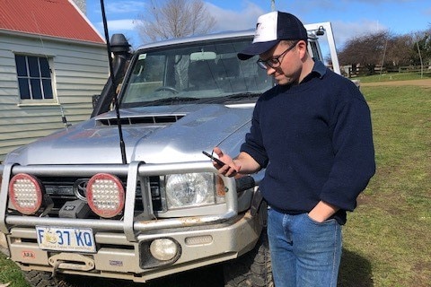 A farmer stands in front of his ute and looks at his iphone