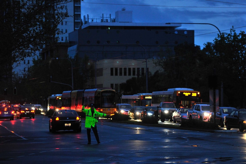 Police direct traffic with light sticks around the CBD in Adelaide under darkness.