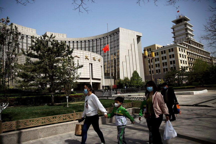 People wearing face masks walk past the headquarters of Chinese central bank People's Bank of China (PBOC)