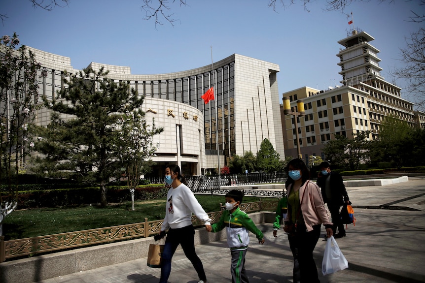 People wearing face masks walk past the headquarters of Chinese central bank People's Bank of China (PBOC)