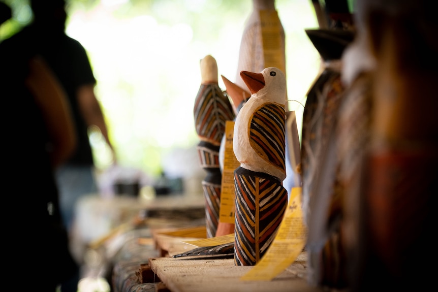 A wooden carving of a bird sits on a table surrounded by other pieces.