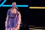 Musician P!nk sings into a microphone on stage wearing an embellished gown with feathery sleeves.