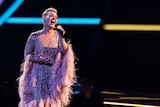 Musician P!nk sings into a microphone on stage wearing an embellished gown with feathery sleeves.