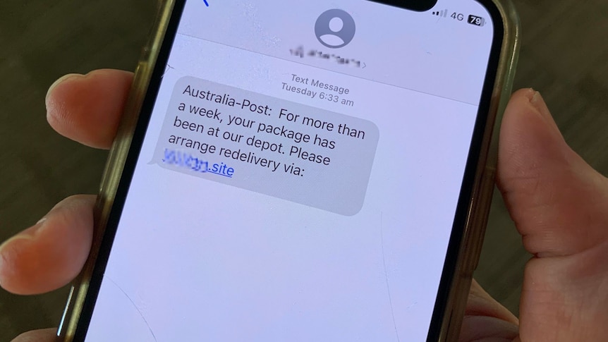 A hand holds a smartphone with a text message claiming to be from Australia Post, asking to arrange a 'redelivery' 