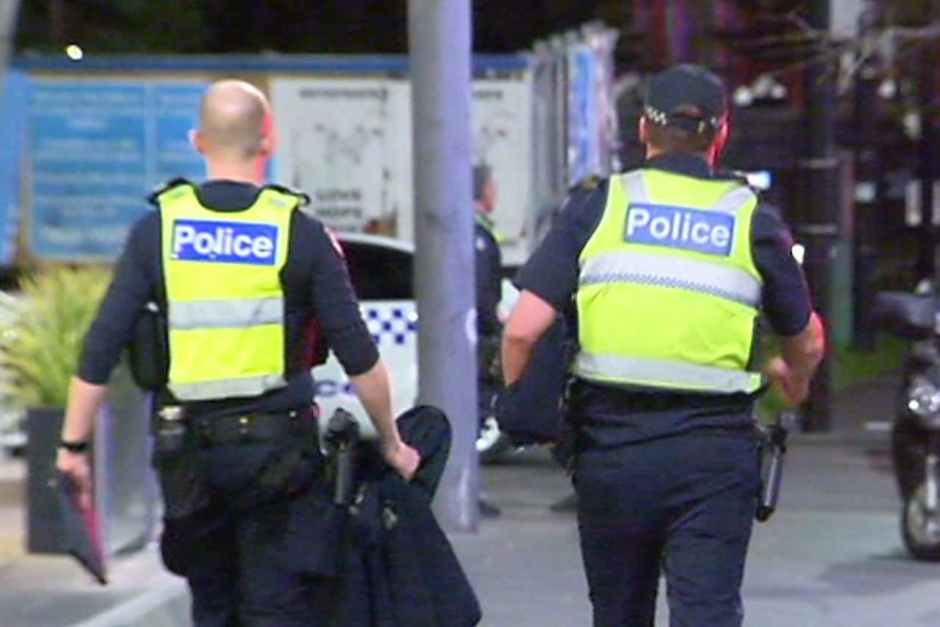 Two police officers holding gear walk down a street at night.