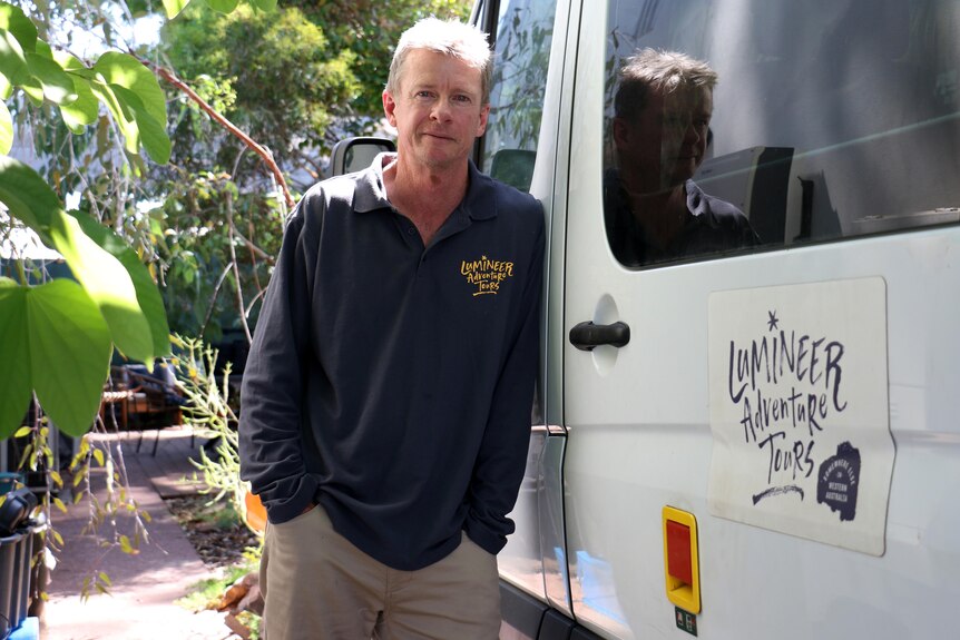 Mr Parker leans against a tour bus, with the words "Lumineer Adventure Tours" written on it.