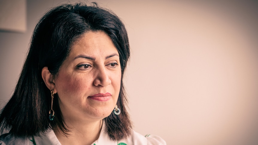 A woman with shoulder length dark hair looks solemnly into the distance.