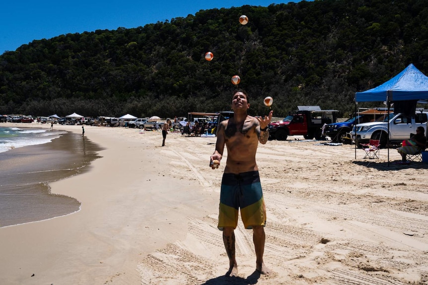 A man juggles balls on the beach at Double Island Point that is packed with four-wheel drive Vehicles and sun shades.