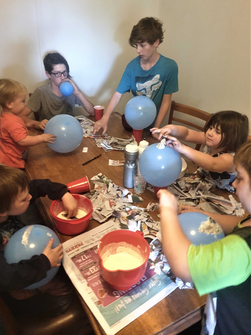 Six children around a table with balloons and newspaper.