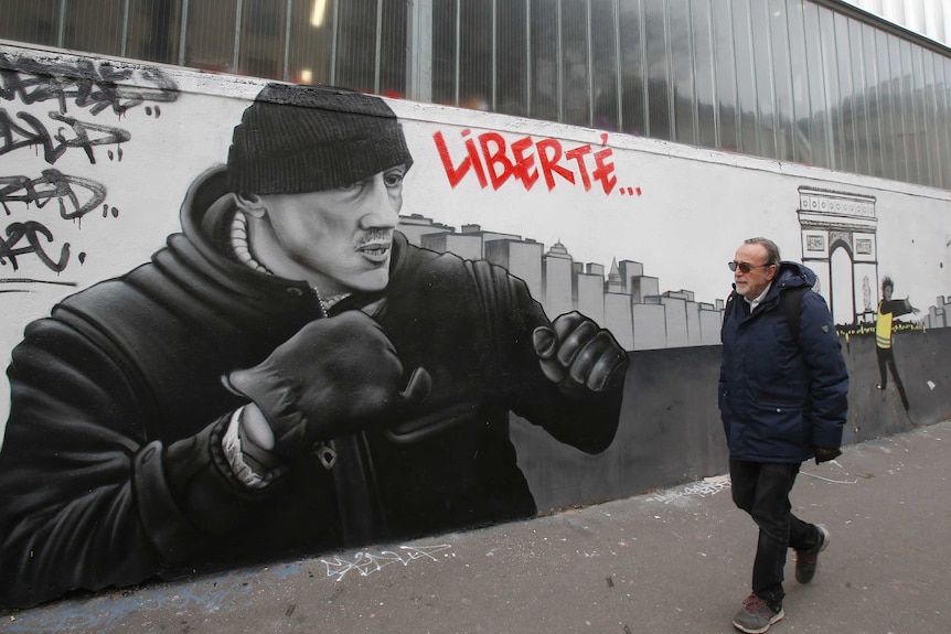 A man walks past a mural of a boxer painted on a street wall.