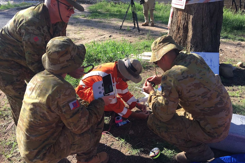 Men in army and SES uniforms crowd around a drone