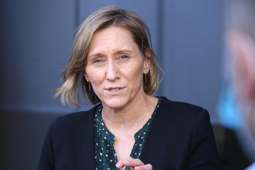 A middle-aged woman with shoulder length hair, wearing a dark outfit.