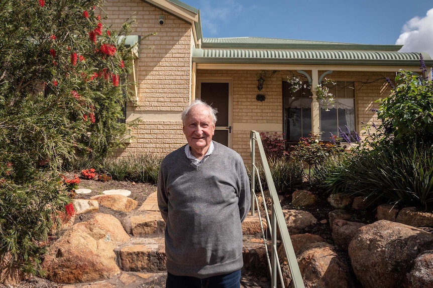 Older man stands in front of brick house and garden