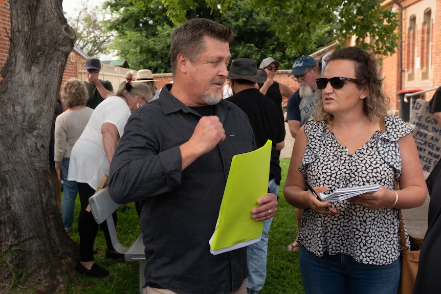 A man wearing a black shirt talks to a woman outside a courthouse.