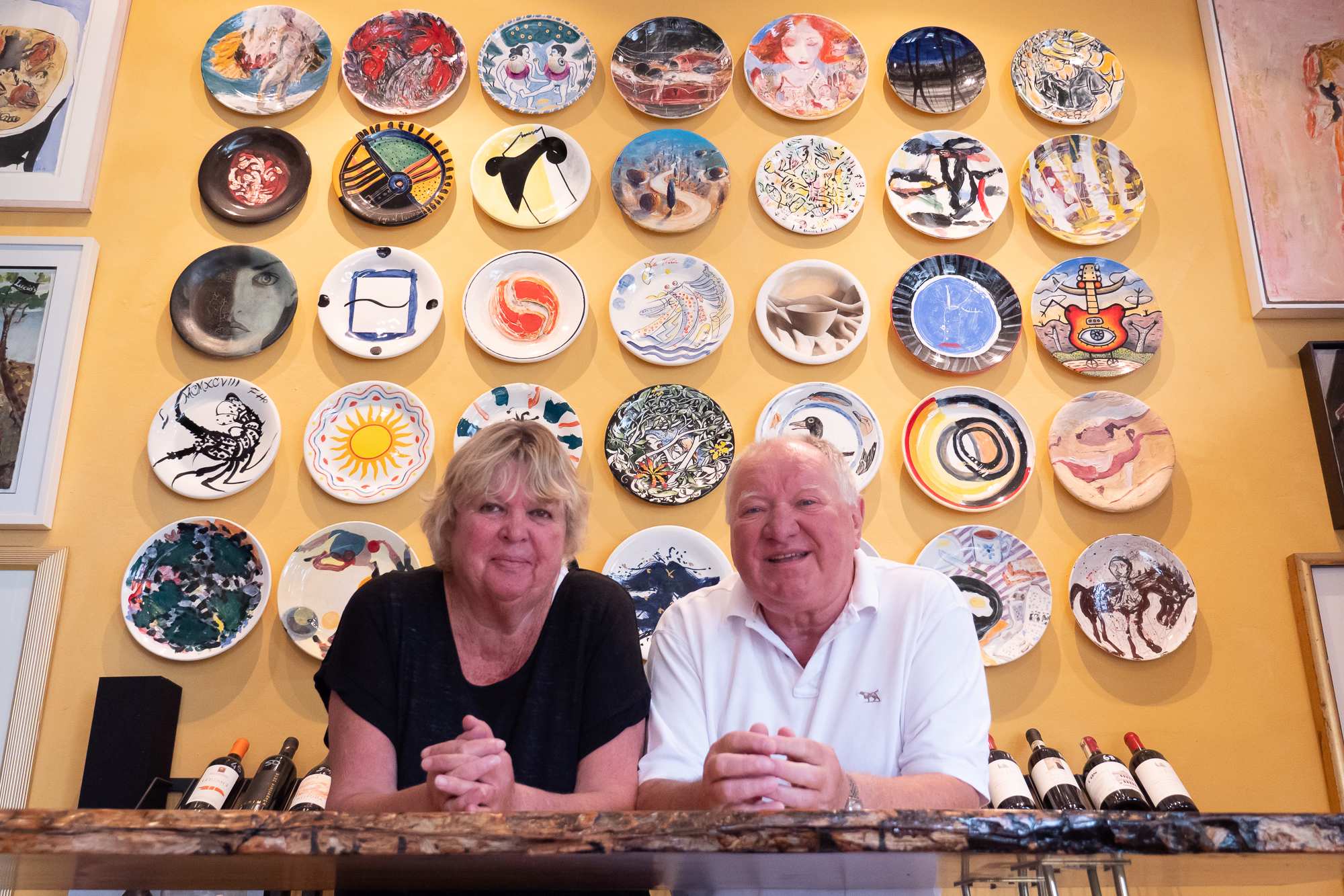 Sally and Lucio Galletto standing in front of a wall of art plates