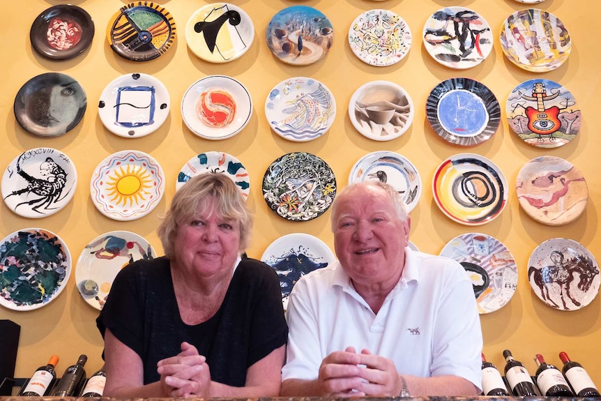Sally and Lucio Galletto standing in front of a wall of art plates