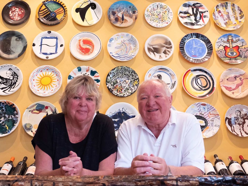Sally and Lucio Galletto standing in front of a wall of art plates
