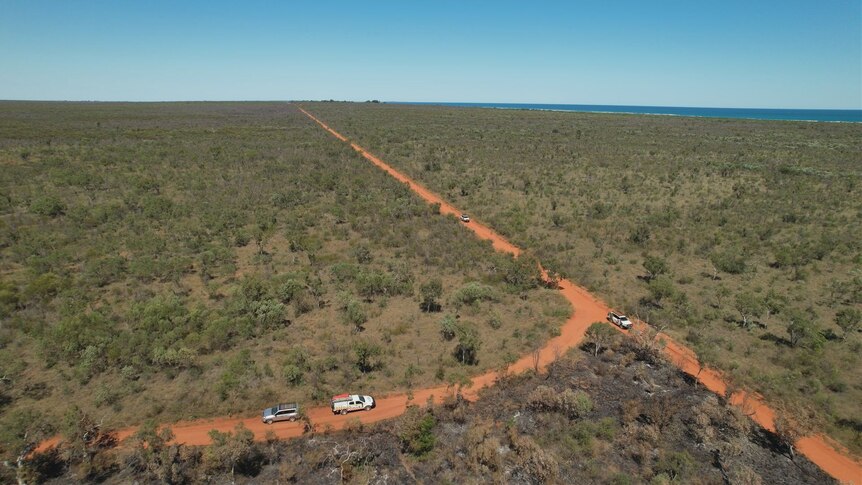 An aerial shot of vehicles on a dirt track surrounded by bushland.