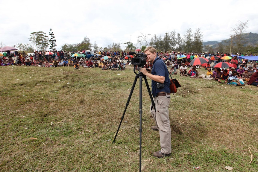 Liam Fox filming with camera surrounded by villagers.