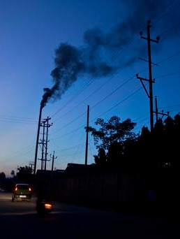 Traffic moves as smoke emits from the chimney of a factory on the outskirts of Gauhati, India.