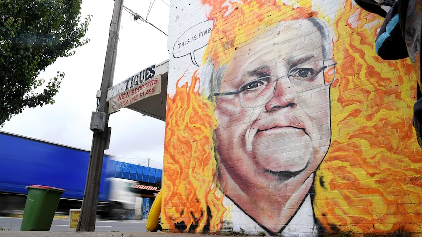 Scott Morrison is painted on a wall surrounded by flames, with a speech bubble that says 'this is fine'.