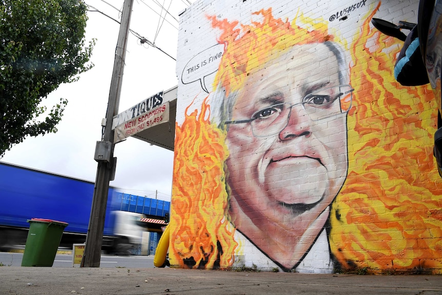 Scott Morrison is painted on a wall surrounded by flames, with a speech bubble that says 'this is fine'.