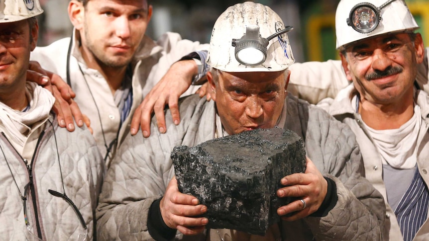 A miner kisses a piece of coal as his colleagues huddle around him.