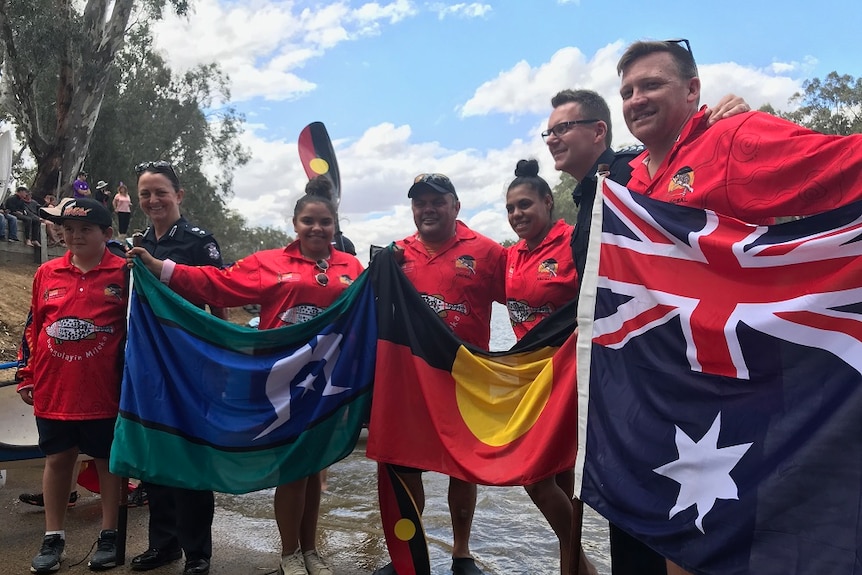 Victoria police officers and Indigenous people group together holding Torres Strait Islander, Indigenous and Australian flags.