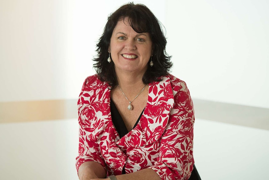 A portrait photograph of a dark-haired woman wearing a bright red, patterned jacket over a black dress