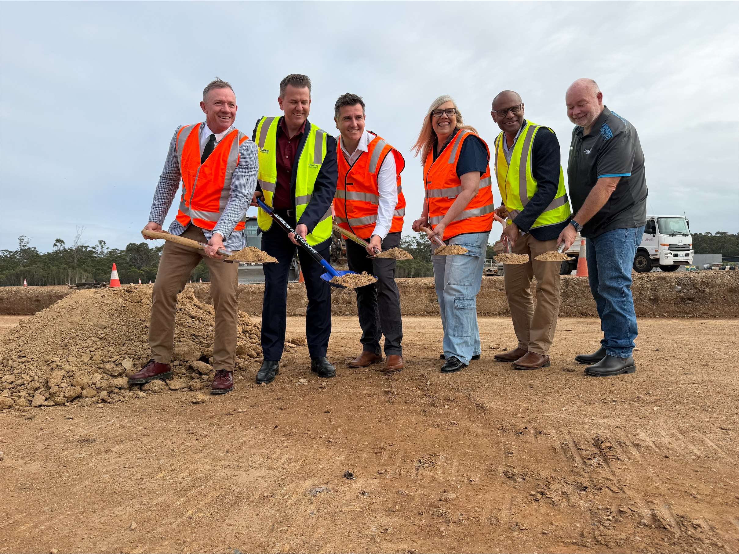 People in high vis holding shovels of dirt on a work site