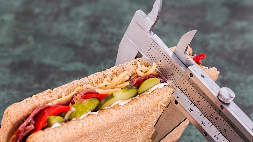 A crispbread sandwich containing salad and cheese being measured in inches.