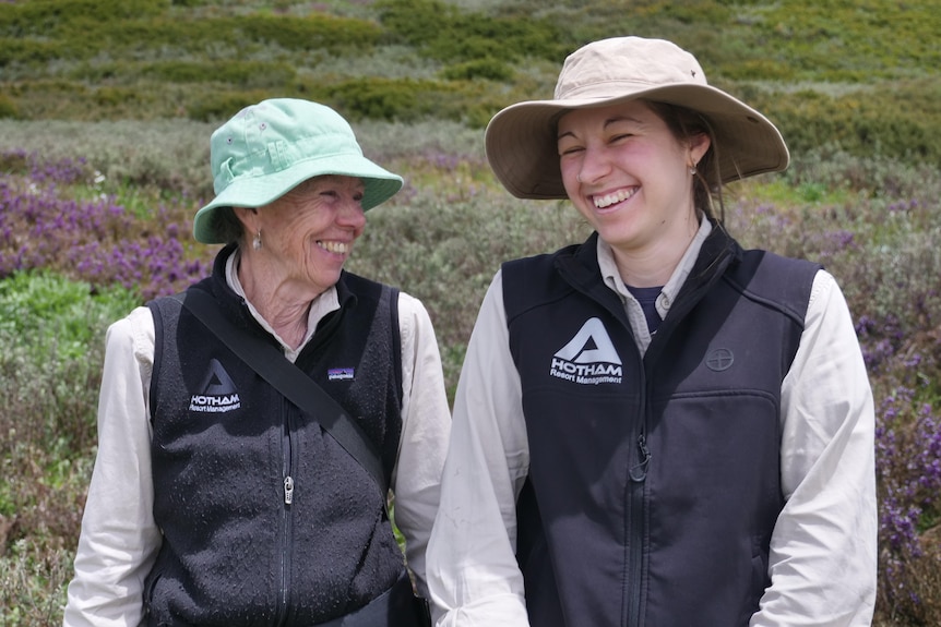 Two women laugh together with native wildflowers in the backgrounds