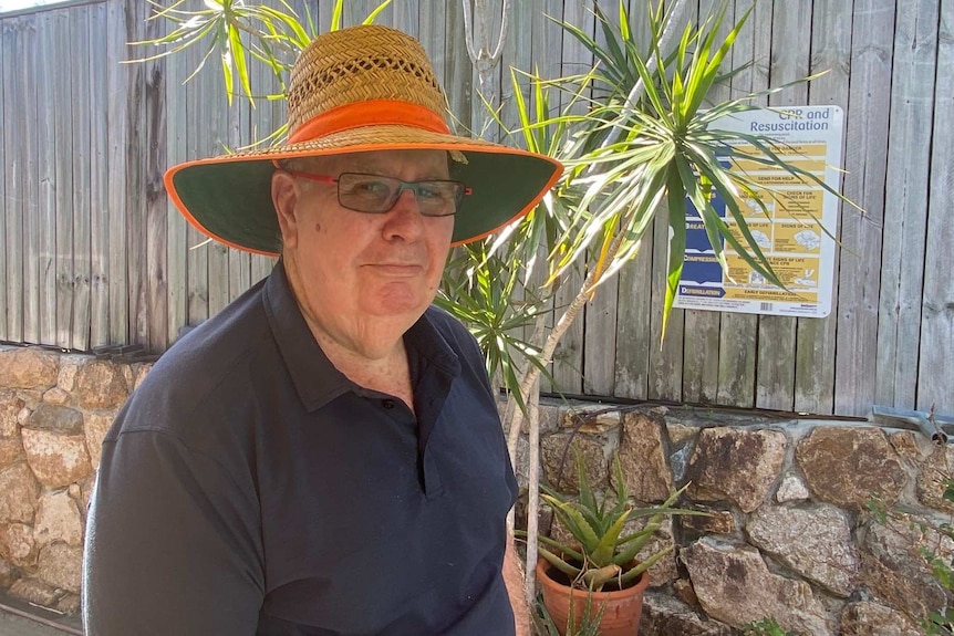 Man with big hat stands under an awning in his garden